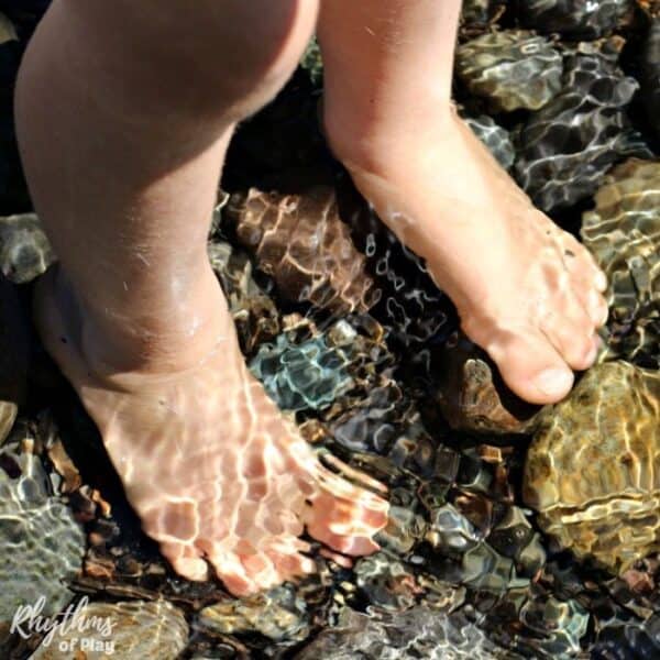Preschool aged kid barefoot outside with feet in the creek water standing on stones. (Photograph of Charlize Kartychok by Nell Regan K.)