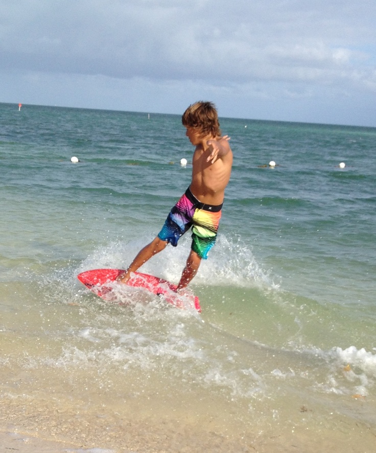 This may contain: a young man riding a surfboard on top of a wave in the ocean,