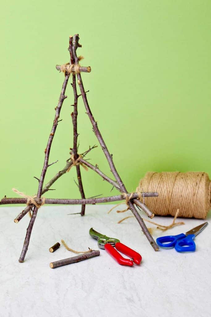 Completed tabletop easel from twigs against a green background.