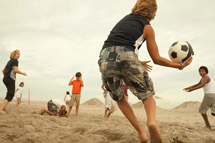 This may contain: a group of people playing soccer on the beach with sand and sky in the background