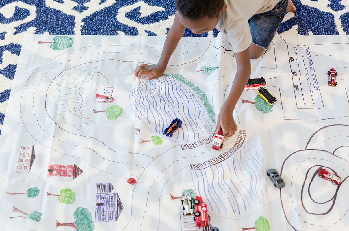 A boy playing on a shower curtain liner that has drawings of a town and roads on it.