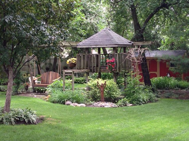 This may contain: a garden with a wooden gazebo surrounded by lush green grass