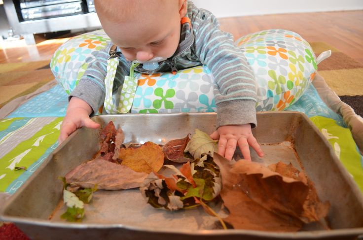 This may contain: a toddler playing with leaves in a metal pan on the floor at christmas time