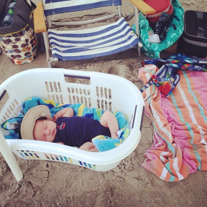 This may contain: a baby laying in a laundry basket on the beach