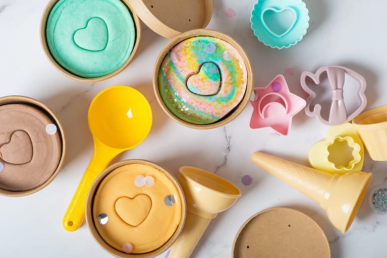 Containers of pastel-colored play dough and play dough tools.