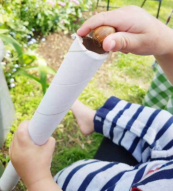 Loose parts play, baby enjoying how hazelnuts fall through a tube