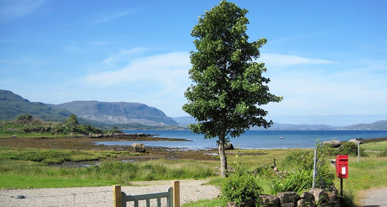 a sunny day in the highands, with a path leading onwards to mountains, water and greenery