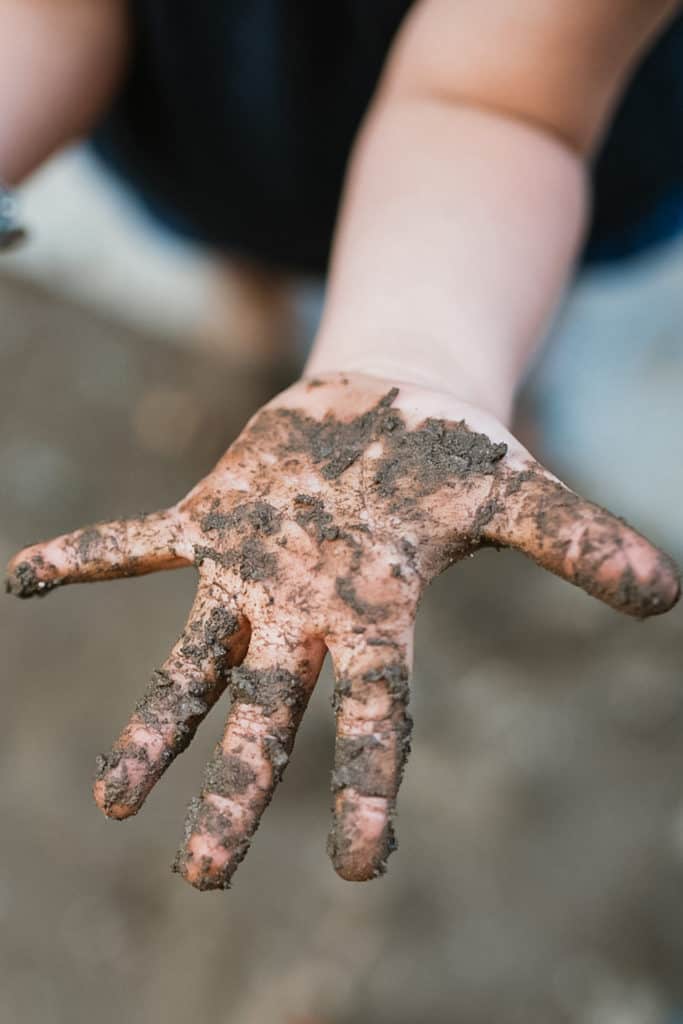 An 18-month-old toddler's outstretched hand covered in mud from doing an outdoor learning activity.