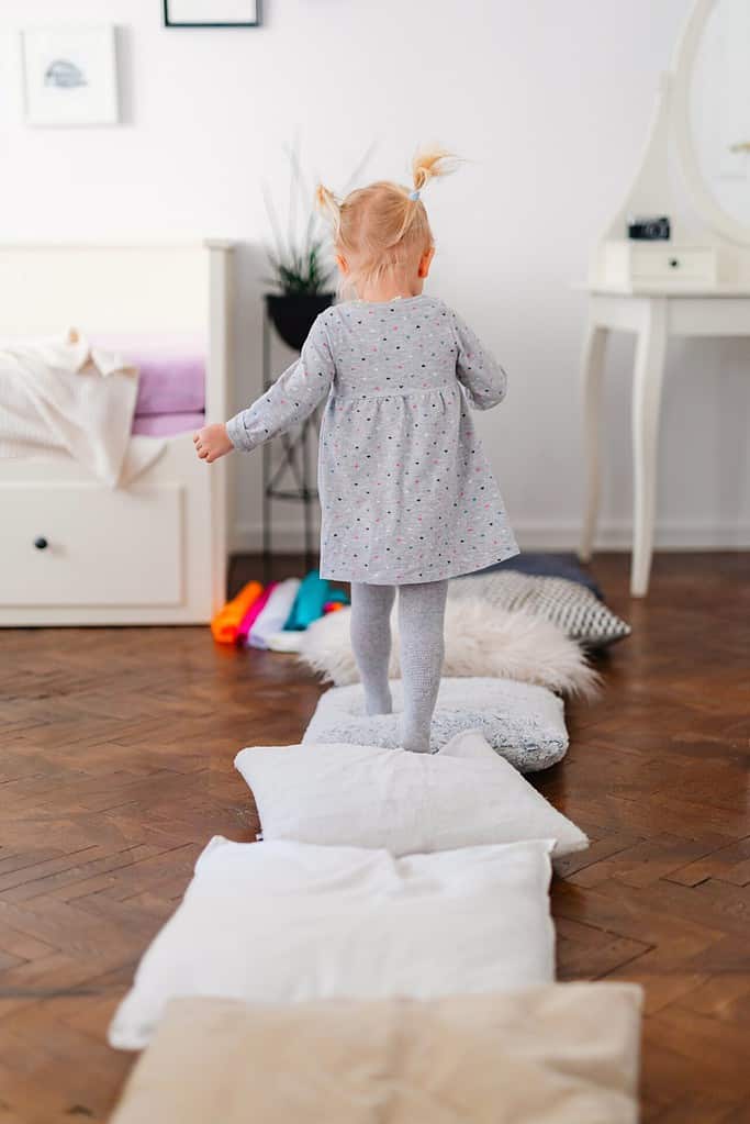 An 18-month-old toddler walks across pillows during a sensory walk.