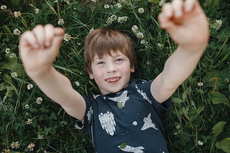 A child lies on the grass and reaches for the camera.