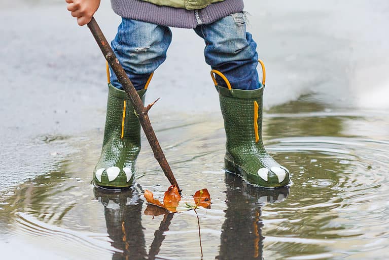 Child with rainboots jumping in a puddle on a rainy day.