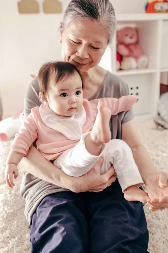 Grandparent holding a baby and touching babies feet during a sensory play activity.