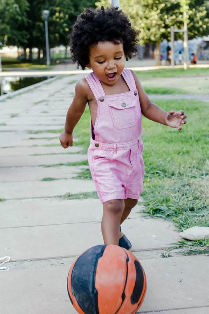 A toddler chasing a ball down the sidewalk at a park during outdoor play.