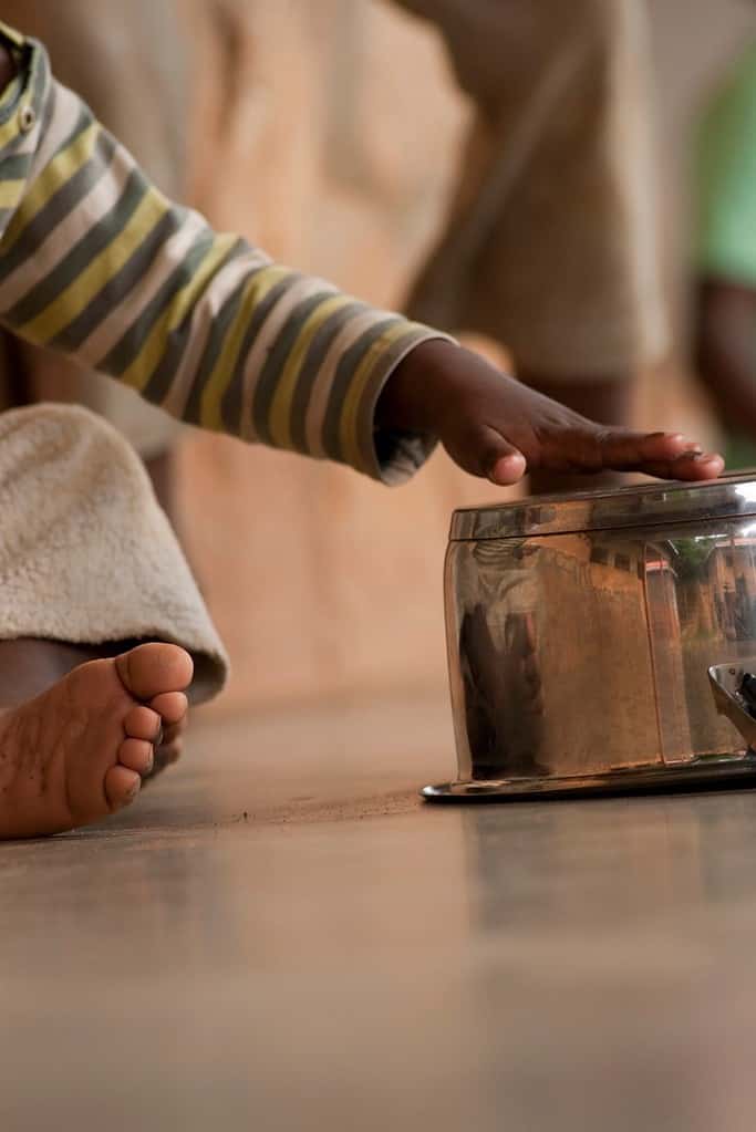 An 18-month-old toddler taps their hand on a metal pan during a sensory learning activity.