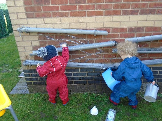 Pre-school children in red and blue rpuddlesuits playing with guttering