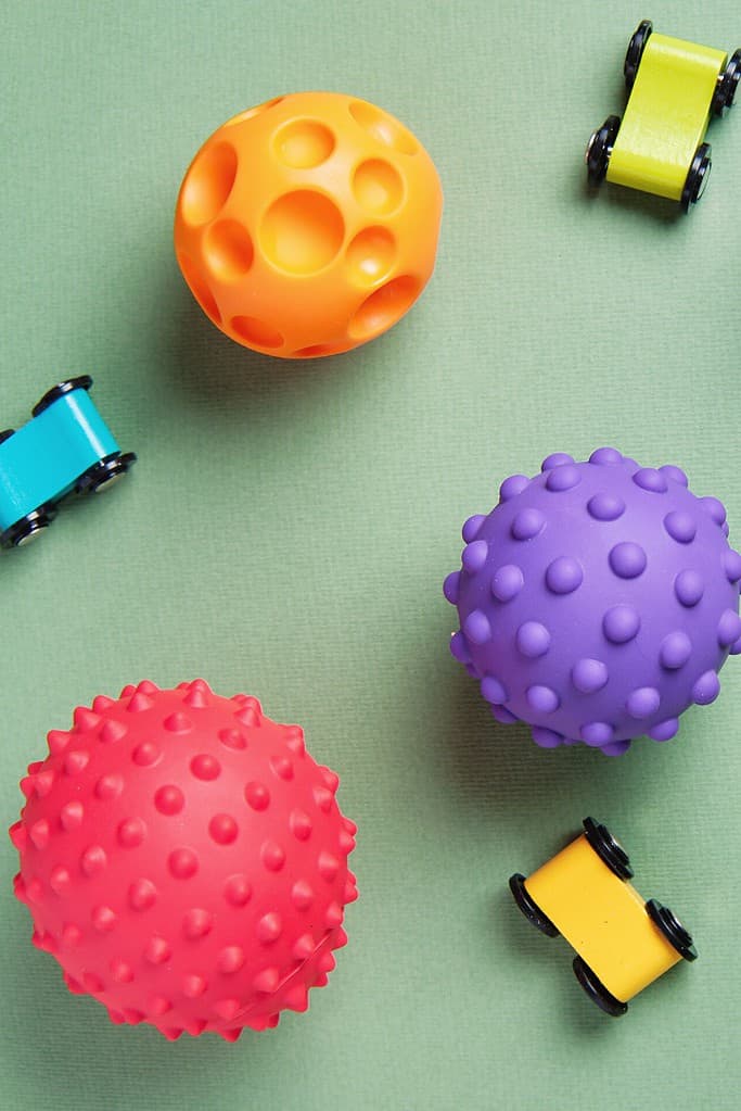 Colorful textured balls and wooden cars for sensory learning activities for 18-month-olds.