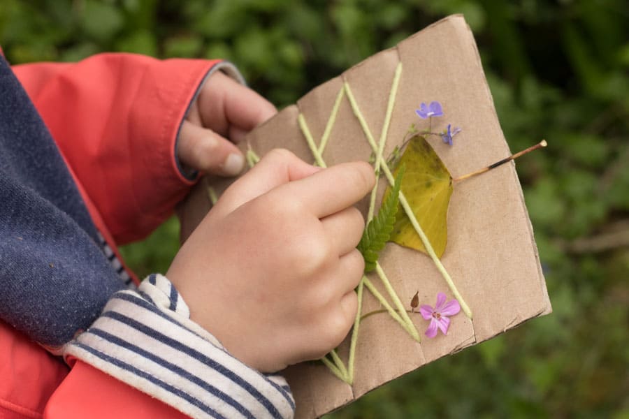 Child's hands adding nature to a piece of card board with wool wrapped around it