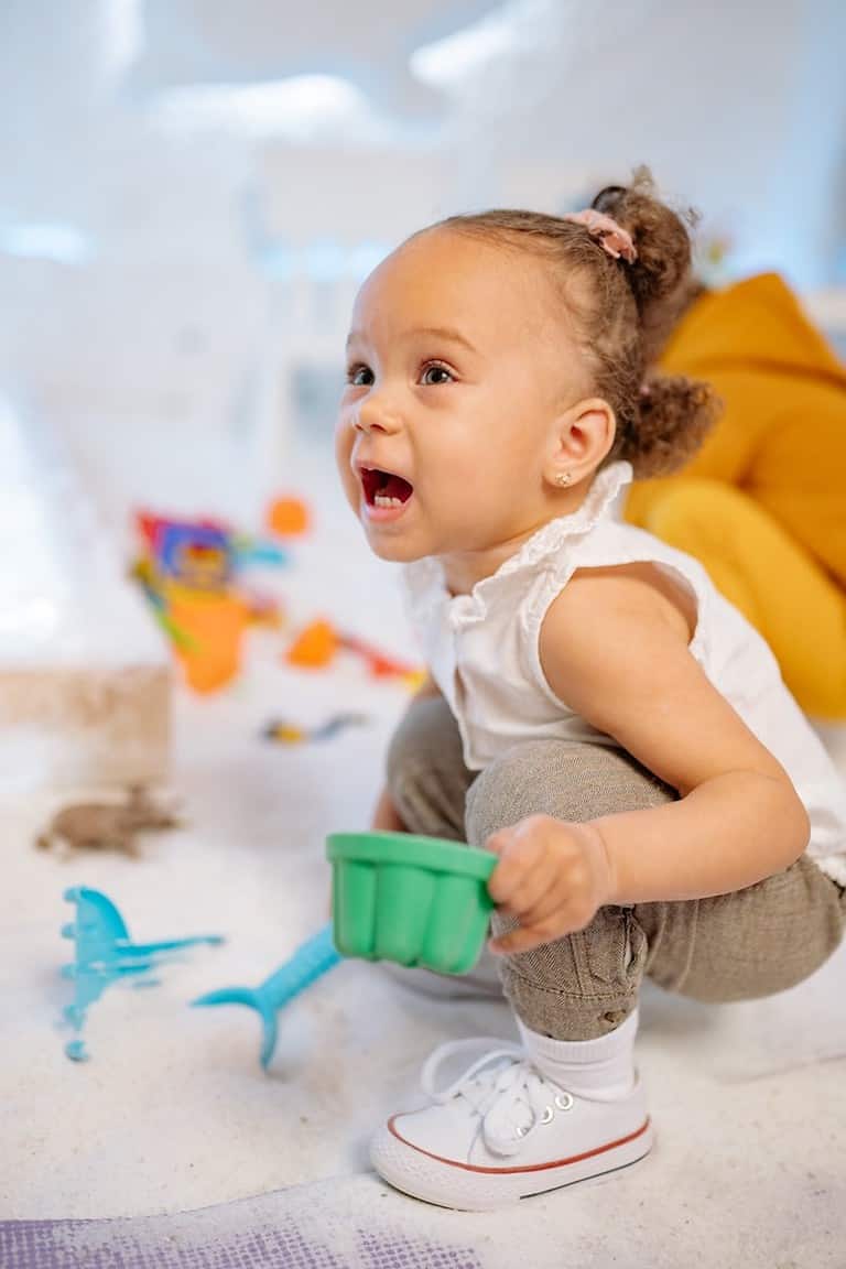 A toddler plays in a sand table during an interactive learning activity.