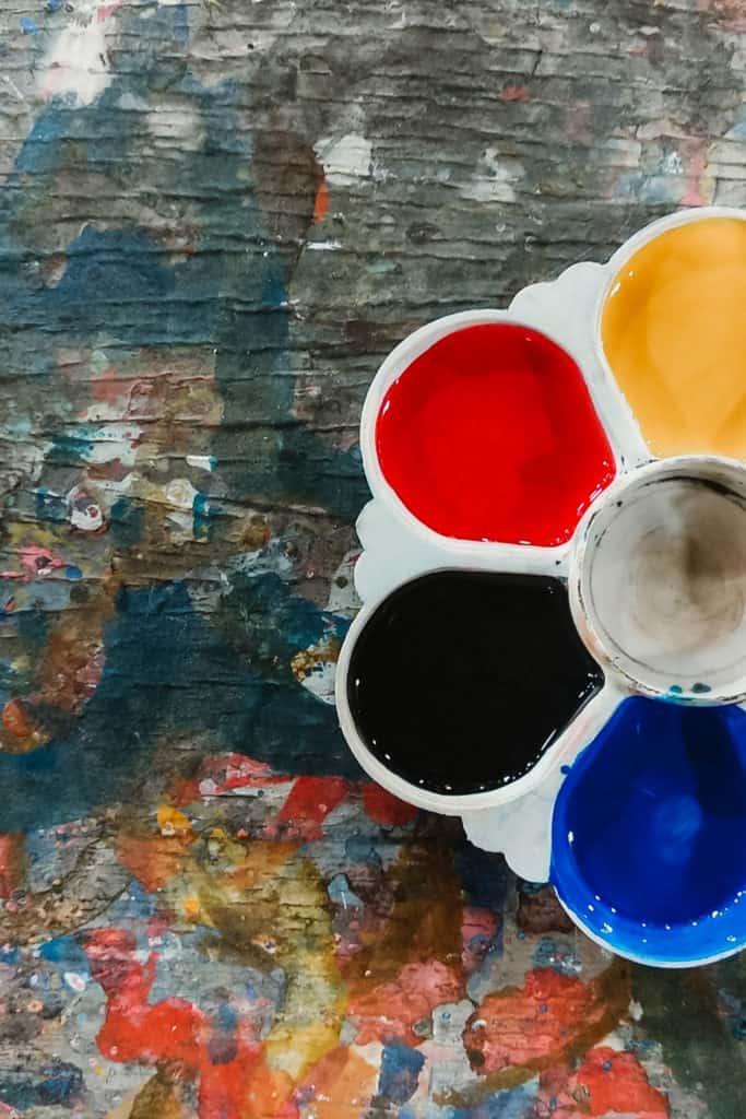 Watercolor paints on a paint covered table that toddlers could use during an outdoor learning activity.