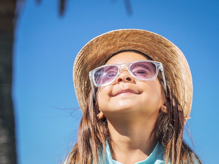 A child wears a hat and sunglasses on the beach in summer.