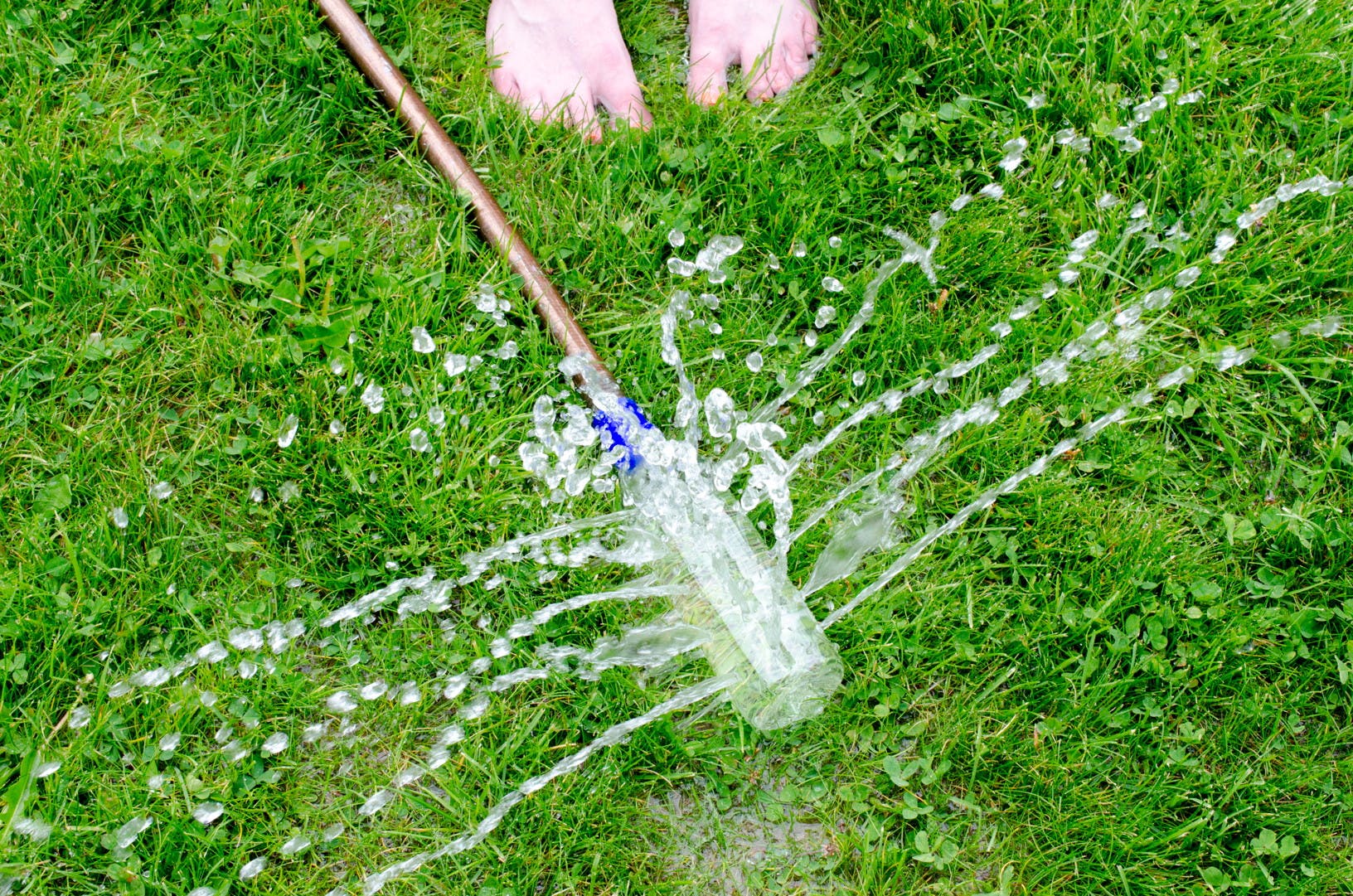 A water bottle with holes drilled into it that has been attached to a hose to make a DIY sprinkler