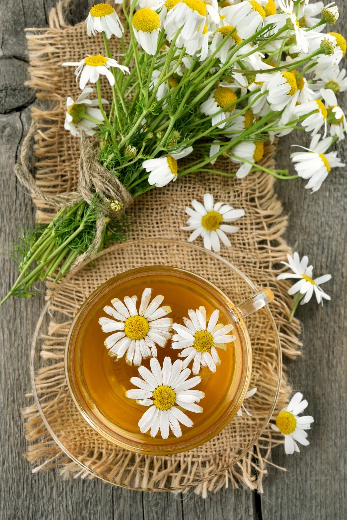 Herbal tea with chamomile in glass cup on wooden table, top view.