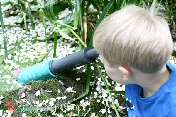 a boy looking through an aquascope (recommended on the best biology kits for kids) to see what is happening in a nature pond.