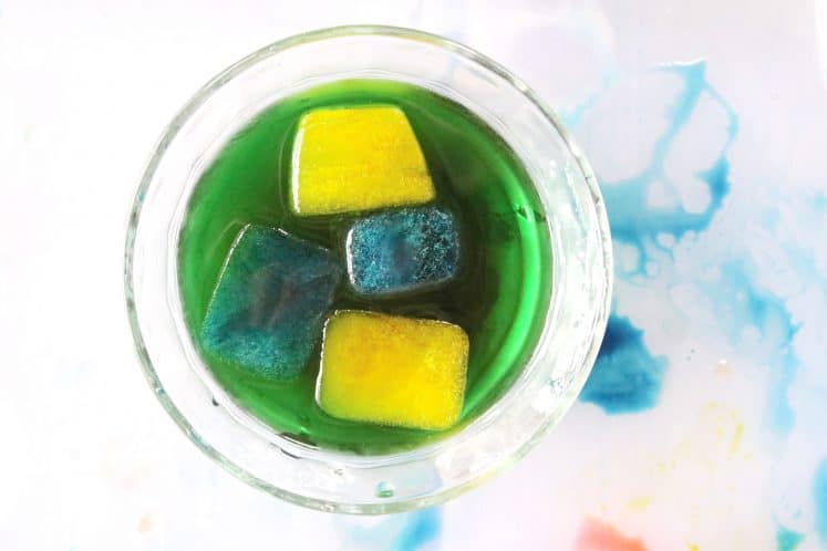 dish of green water containing yellow and blue ice cubes