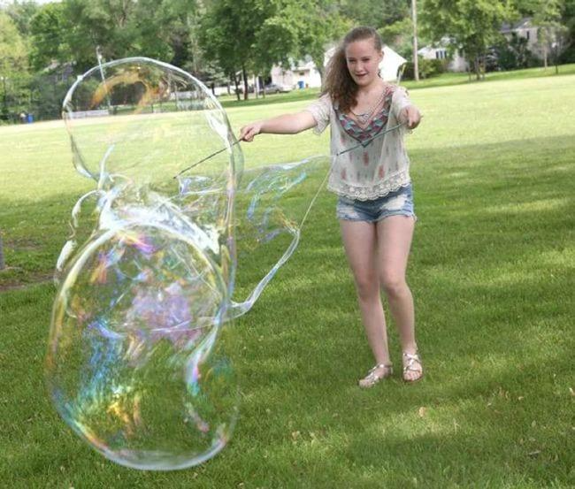 Student creating an enormous soap bubble with string on sticks (Outdoor Science)